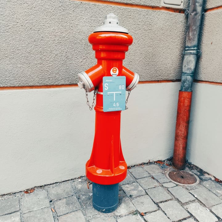 Roter Überflurhydrant mit Hydrantenschild an einer Hauswand